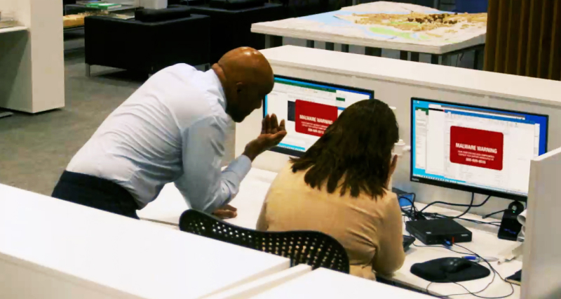 Two people seen from behind looking at computer screens with ransomware messages due to an infected USB drive. This may have been the situation with the ransomware attack on Garmin.