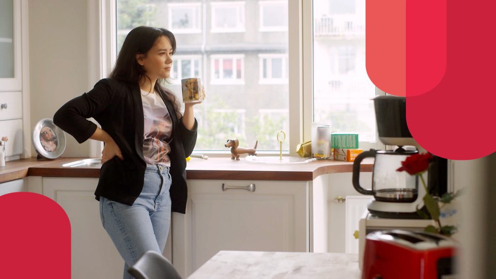 Still from our cybersecurity videos about spear phishing. A woman stands in kitchen holding a cup of coffee. All around is dachshund memorabilia to show her special interest in a specific dog breed.