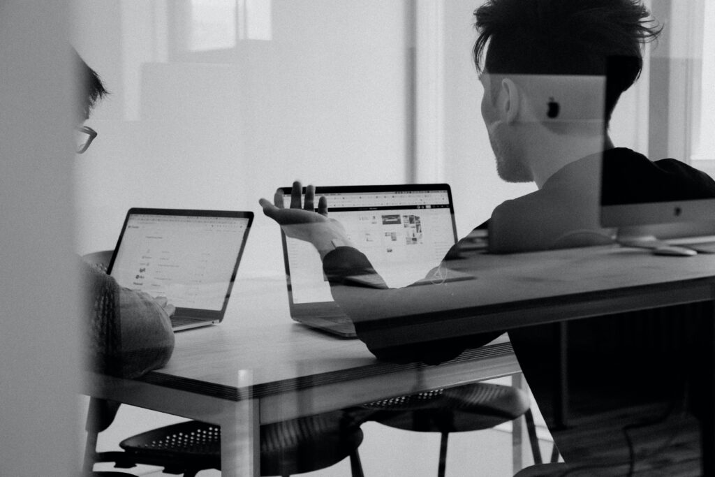 Black and white photo with two men sitting at a desk and looking at their computers learning about information security awareness